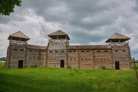 Foto de Una antigua fortaleza de madera rodeada por una cerca con picos afilados en un día lluvioso brumoso. Casa de madera en un estilo rústico. - Imagen libre de derechos