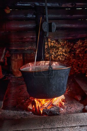 Photo for A large vat in which cheese is cooked over an open fire. The black cauldron is prepared over an open wood fire. Cheese factory in the mountains. - Royalty Free Image
