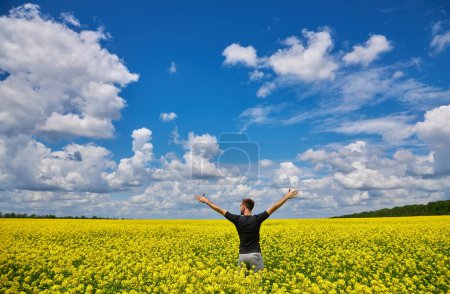 Foto de Attractive man with arms outstretched. Handsome young man standing in a field of blooming yellow rapeseed flowers. - Imagen libre de derechos