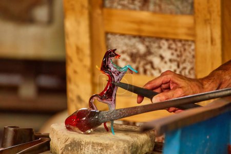 Foto de Un soplador de cristal de Murano sostiene una escultura de caballo de cristal caliente rojo - Imagen libre de derechos