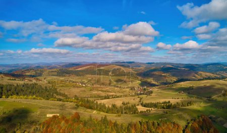 Téléchargez les photos : Vue aérienne des montagnes au lever du soleil en automne en Ukraine. Paysage coloré avec route de montagne, forêt, maisons sur les collines, lumière du soleil, ciel en automne. Vue du dessus de la route et du village - en image libre de droit
