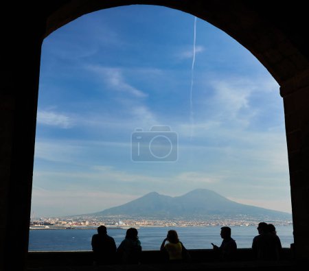 Téléchargez les photos : La silhouette d'un groupe de touristes, regardant le Vésuve depuis le château d'Egg à Naples par une journée ensoleillée. - en image libre de droit