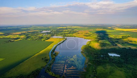 Téléchargez les photos : Vue aérienne de la large rivière qui coule tranquillement dans la campagne rurale entre les champs verts en soirée d'été - en image libre de droit