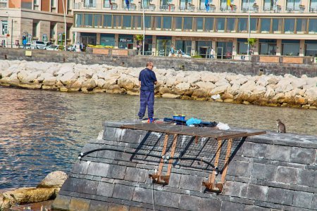 Téléchargez les photos : Naples, Italie - 24 octobre 2019 : Pêcheur avec chat sur la jetée de la promenade de Via Nazario Sauro, Campanie, Italie - en image libre de droit