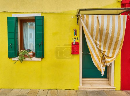 Téléchargez les photos : Porte et fenêtre avec des fleurs sur la façade jaune de la maison. Architecture colorée sur l'île de Burano, Venise, Italie. - en image libre de droit