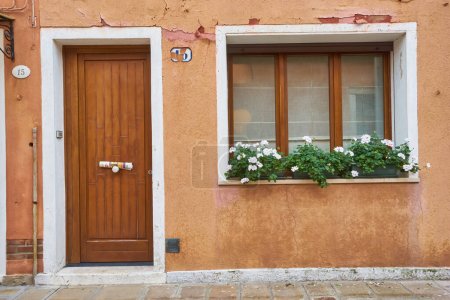 Téléchargez les photos : Porte et fenêtre avec des fleurs sur la façade jaune de la maison. Architecture colorée sur l'île de Burano, Venise, Italie. - en image libre de droit