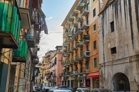 Téléchargez les photos : Naples, Italie - 25 octobre 2019 - Les résidents marchent entre les voitures garées sur une étroite rue bordée de blanchisserie du centre-ville historique de Centro Storico. - en image libre de droit