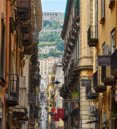 Photo for Naples, Italy - October 25, 2019 - Residents walk between cars parked on a narrow laundry-lined street of the historic Centro Storico city center. - Royalty Free Image