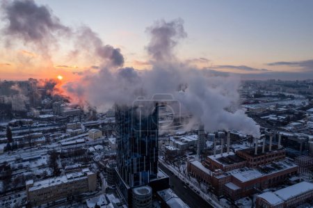 Téléchargez les photos : Silhouette d'un grand vieux tuyau avec un nuage de vapeur contre un coucher de soleil bleu d'hiver. Une chaufferie de grande ville fonctionne à pleine capacité - en image libre de droit