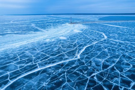 Téléchargez les photos : Vue aérienne d'un phare solitaire dans la mer gelée. Glace bleue gelée dans les fissures, vue sur drone - en image libre de droit