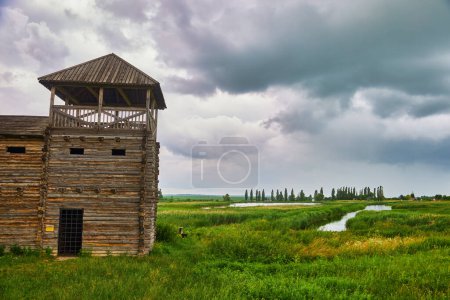 Téléchargez les photos : Une vieille forteresse en bois entourée d'une clôture avec des pics pointus par un jour de pluie brumeux. Maison en bois dans un style rustique. - en image libre de droit