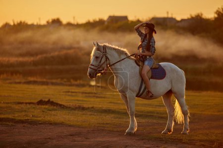 Foto de Hermosa joven con pelo largo en sombrero de vaquero con el caballo marrón al aire libre en la naturaleza - Imagen libre de derechos