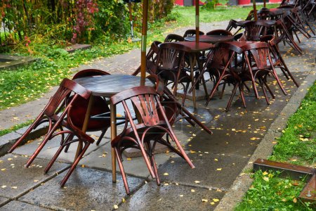 Téléchargez les photos : Chaises en bois appuyées sur des tables dans un café ou un restaurant fermé le matin après la pluie - en image libre de droit