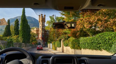 Téléchargez les photos : Vue d'une vieille ville italienne dans les Alpes à travers le pare-brise d'une voiture. La ville est située au sommet d'une montagne et est entourée de sommets imposants. Les rues de la ville sont bordées de petites maisons, magasins et restaurants. - en image libre de droit