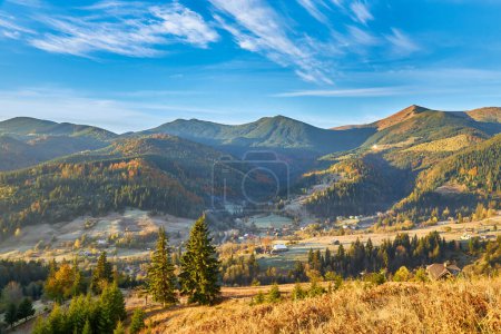 Foto de Un paisaje majestuoso: hojas amarillas, bosques de coníferas y deciduos rodean un pueblo pacífico en una mañana de otoño en las montañas - Imagen libre de derechos