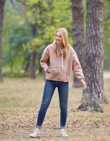 Photo for Beautiful young blonde woman in beige hoodie walks in the park. Attractive female spending active time in the park. Portrait of a joyful young woman enjoying in autumn park. Relax in nature. - Royalty Free Image