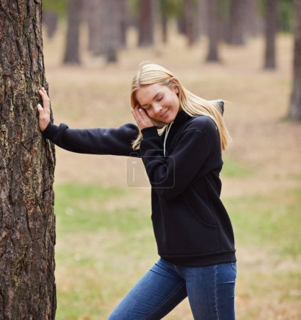 Photo for Blue-eyed blonde in a black hoodie walks in a pine forest. Portrait of a joyful young woman enjoying in autumn park. Relax in nature. - Royalty Free Image