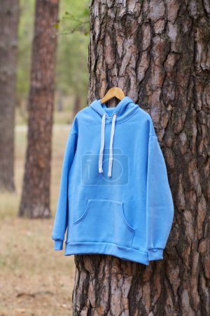 Photo for Blue hoodie hanging on a hanger on a tree in the forest. Demonstration of different colors of clothes - Royalty Free Image