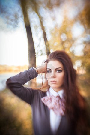 Photo for In the enchanting autumn forest, a brunette girl stands, captivated by the serene beauty surrounding her. The golden sunlight filters through the colorful canopy, casting a warm glow on her. - Royalty Free Image