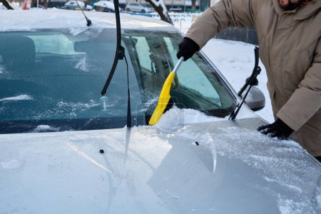 Photo for A man clearing snow from a car using a brush on a cold winter day, showcasing the routine task of snow removal - Royalty Free Image