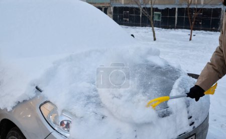 Téléchargez les photos : Au milieu de l'hiver, un homme balaie avec diligence la neige de sa voiture, une scène typique reflétant la nécessité du déneigement pour assurer des conditions de conduite sécuritaires. - en image libre de droit
