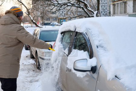 Téléchargez les photos : Au milieu de l'hiver, un homme balaie avec diligence la neige de sa voiture, une scène typique reflétant la nécessité du déneigement pour assurer des conditions de conduite sécuritaires. - en image libre de droit