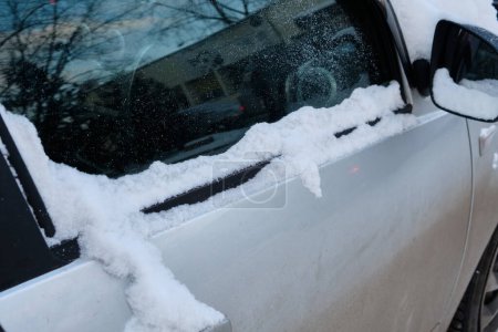 Téléchargez les photos : Une voiture garée dans la neige, sa fenêtre recouverte d'une épaisse couche de neige, créant une scène hivernale au pays des merveilles et soulignant le temps froid. - en image libre de droit