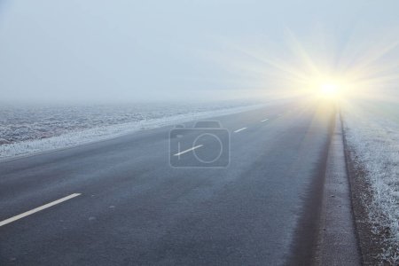 Téléchargez les photos : Le matin d'hiver. Le brouillard dérive sur les arbres couverts de givre blanc. Une bonne route asphaltée mène au loin et disparaît dans le brouillard. - en image libre de droit