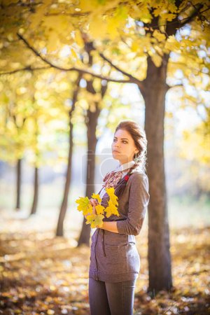 Téléchargez les photos : Dans la forêt d'automne enchanteresse, une fille brune se tient debout, captivée par la beauté sereine qui l'entoure. Le soleil doré filtre à travers la verrière colorée, projetant une lueur chaude sur elle. - en image libre de droit