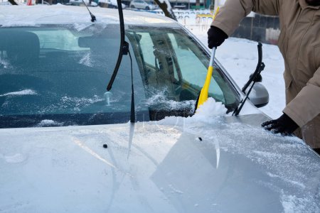 Photo for Amidst winter, a man diligently brushes off snow from his car, a typical scene reflecting the need for snow removal to ensure safe driving conditions. - Royalty Free Image