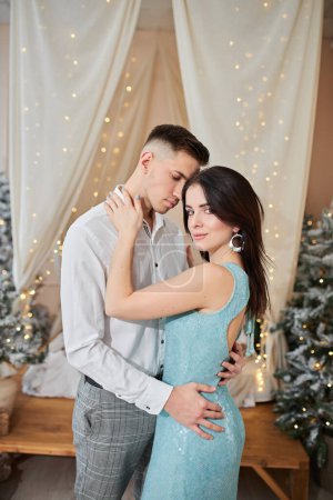 Photo for Young couple in love stands near the Christmas tree and hugs - Royalty Free Image