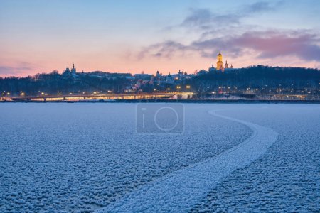 Foto de Mientras el sol se pone en una noche de invierno, el río Dnipro en Kiev se transforma en una obra maestra congelada y brillante, que ofrece una vista impresionante de la icónica Kiev Pechersk Lavra - Imagen libre de derechos