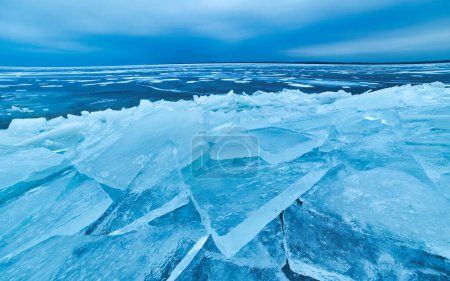 Téléchargez les photos : Une scène hivernale captivante où la glace bleue immaculée étreint le bord de l'eau, superposant délicatement le rivage dans son étreinte cristalline - en image libre de droit