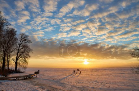 Photo for A captivating winter scene with a frozen lake under the enchanting hues of the setting sun. The sky is ablaze with vibrant colors, casting a serene glow over the icy landscape - Royalty Free Image