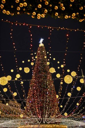 Foto de Gran hermoso árbol de Navidad con decoraciones e iluminaciones en la noche nevada. Año Nuevo y fondo de vacaciones de Navidad. Paisaje festivo invierno ciudad. - Imagen libre de derechos