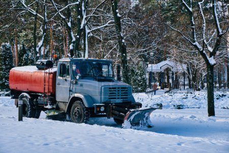 Téléchargez les photos : Une journée d'hiver ensoleillée dans le parc de la ville, où un chasse-neige nettoie efficacement la neige des trottoirs. Les arbres enneigés créent une scène pittoresque. - en image libre de droit