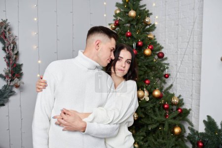 Foto de Joven pareja enamorada se para cerca del árbol de Navidad y abraza - Imagen libre de derechos