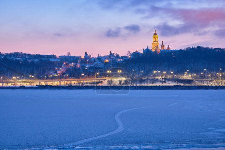 Photo for As the sun sets on a winter's evening, the Dnipro River in Kyiv transforms into a frozen, glistening masterpiece, offering a breathtaking view of the iconic Kyiv Pechersk Lavra - Royalty Free Image