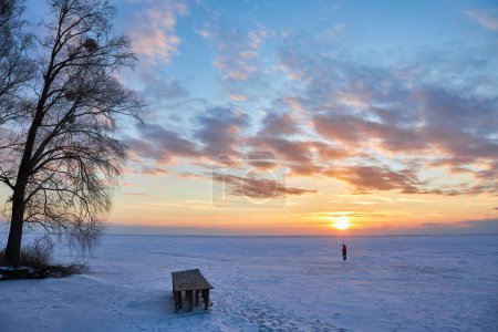 Photo for A captivating winter scene with a frozen lake under the enchanting hues of the setting sun. The sky is ablaze with vibrant colors, casting a serene glow over the icy landscape - Royalty Free Image