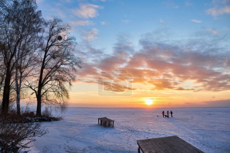 Téléchargez les photos : Une scène hivernale captivante avec un lac gelé sous les teintes enchanteresses du soleil couchant. Le ciel brille de couleurs vives, projetant une lueur sereine sur le paysage glacé - en image libre de droit