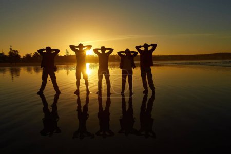 Téléchargez les photos : Des silhouettes de personnes posant contre le ciel du matin créent un paysage de plage captivant. Un groupe de touristes saisit la sérénité de l'aube sur les rives de l'océan Atlantique à Essaouira, au Maroc. - en image libre de droit