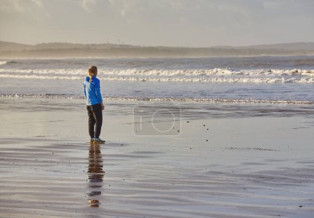 Foto de Una joven disfrutando de un trote costero a lo largo de la costa de Essaouira, con las olas del Atlántico proporcionando un sereno telón de fondo para su vigorizante carrera - Imagen libre de derechos