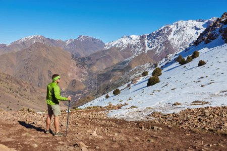 Téléchargez les photos : Un touriste se tient sur le col de l'Atlas, regardant les sommets enneigés, capturant la majesté de cette évasion sereine de montagne. - en image libre de droit