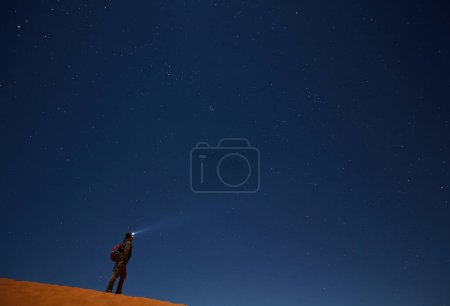 Foto de Un turista con una linterna mira al cielo estrellado sobre el desierto por la noche. - Imagen libre de derechos