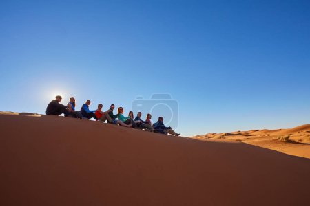 Photo for A group of tourists captures joyful moments, striking playful poses, silhouetted against the mesmerizing backdrop of the Sahara Desert. Morocco. - Royalty Free Image