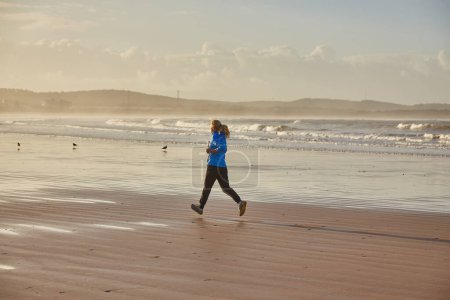 Photo for A young woman embraces the tranquility of a seaside run along Essaouira's ocean, where the rhythmic waves create a soothing backdrop to her invigorating jog - Royalty Free Image