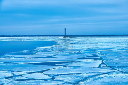 Foto de Una encantadora escena de invierno con un tranquilo embalse, vibrante hielo azul y un faro solitario. - Imagen libre de derechos