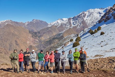 Foto de Un grupo de turistas captura un momento memorable en la cima de las montañas del Atlas en Marruecos, enmarcando el impresionante telón de fondo montañoso - Imagen libre de derechos