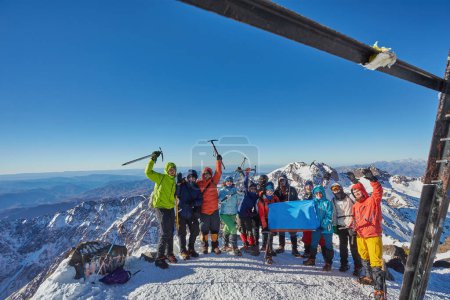 Téléchargez les photos : Un touriste triomphant au sommet du mont Toubkal, au Maroc, célébrant l'ascension avec les mains levées et une hache de glace. - en image libre de droit
