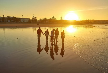 Foto de Los turistas capturan la esencia del amanecer en la playa atlántica de Essaouira, fotografiando recuerdos de siluetas contra el cielo temprano en la mañana.. - Imagen libre de derechos